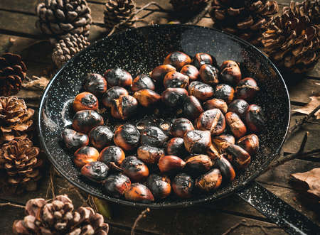 Roasted chestnuts in a chestnut pan (skillet with holes) on a table with autumn leaves and pine cones. Ready to eat. Traditional autumn food.の写真素材