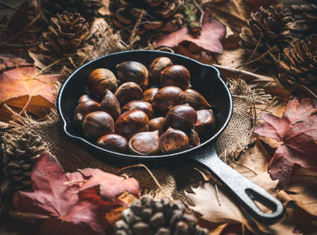 Raw chestnuts in a small iron pan on a table with autumn leaves and pine cones. Ready to roast and eat. Traditional autumn food.の写真素材