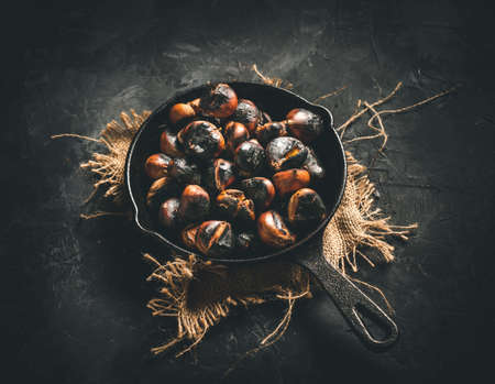 Roasted chestnuts in a small iron pan on a dark table. Ready to eat. Traditional autumn food.の写真素材