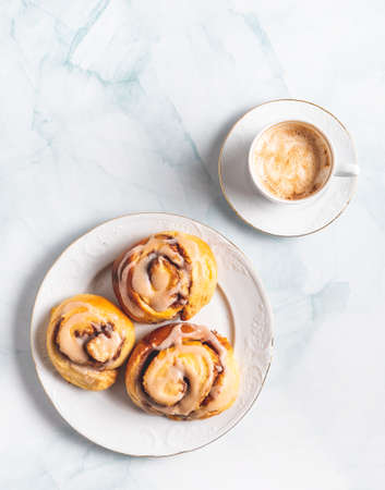 Homemade cinnamon rolls on a white plate and a cup of coffee on a white table. Traditional Swedish and Danish recipe.の写真素材