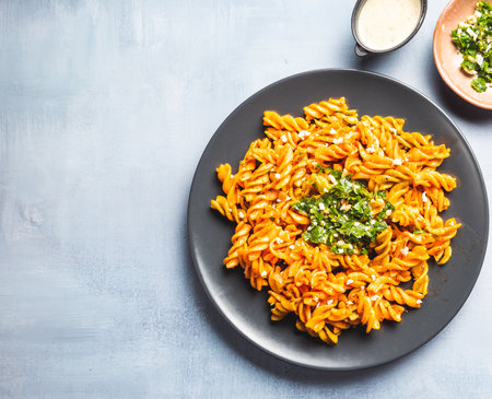 Curly pasta macaroni with tomato and gremolata sauce in a round dark plate on a table. Ready-to-eat.の写真素材