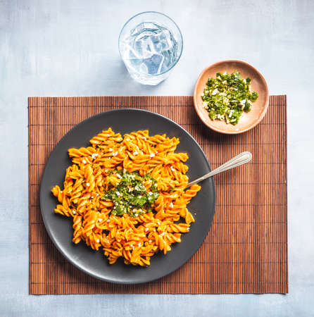 Curly pasta macaroni with tomato and gremolata sauce in a round dark plate on a table with cutlery and a glass of water. Ready-to-eat.の写真素材