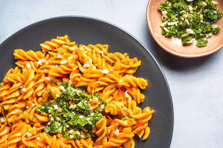 Curly pasta macaroni with tomato and gremolata sauce in a round dark plate on a table. Ready-to-eat.の写真素材