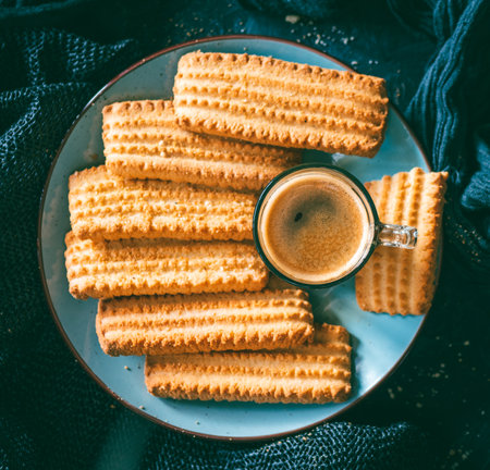 Traditional homemade shortbread cookies called âgalletones manchegosâ on a round blue plate next to a glass cup of coffee on a dark table. Sweet food for breakfast or snack.の写真素材