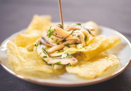 Potato chips with pickled anchovies in a white round plate on a table. Typical Spanish food called...