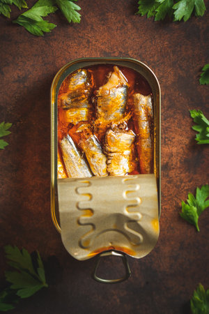Canned sardines with tomato sauce open on a dark brown table with lemon and parsley. Ready to eat.の写真素材