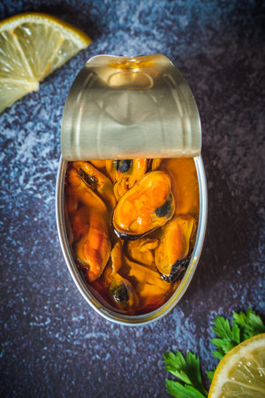 Canned pickled mussels open on a dark blue table with lemon and parsley. Ready to eat.の写真素材