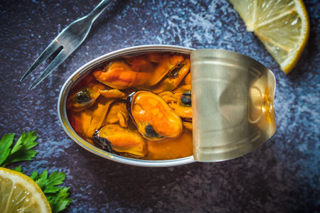 Canned pickled mussels open on a dark blue table with a fork, lemon and parsley. Ready to eat.の写真素材