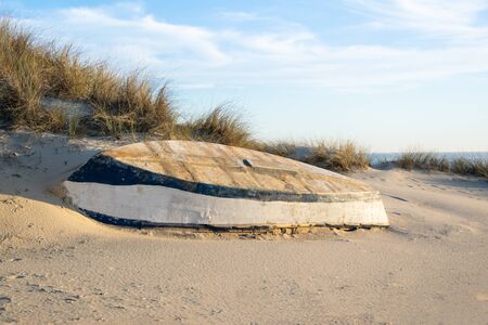 Blue and white wooden boat abandoned on the sand with the sea in the background and the sky with white clouds.の写真素材