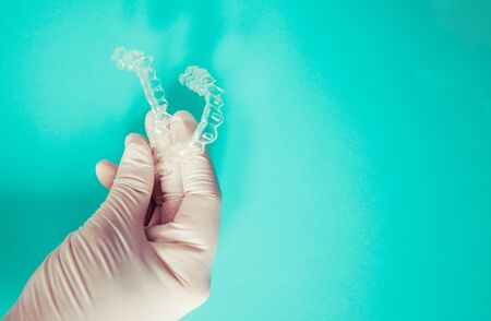 Doctor's hand teaches clear dental aligners on sky-blue background with copy spaceの写真素材