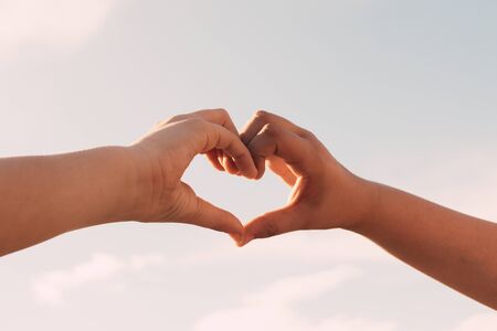 Two sisters joining hands in the shape of a heart in the background of the blue sky, Family