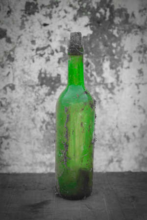 Green Moment, Old Bottle. Old wine bottle, on a desaturated wall background. It is on a table.のeditorial素材