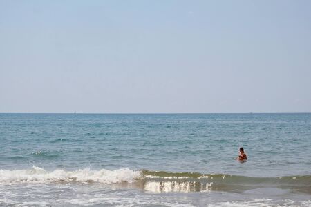 Woman on the sea coast. sunny day. sailboat on the horizonの写真素材