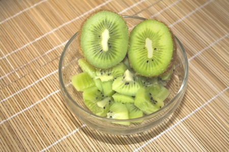 Kiwi sliced on top of a bowl filled with kiwis on a wood tableの写真素材