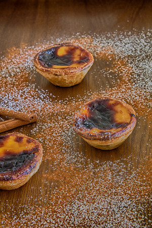 three traditional portuguese egg pies on a wood table with cinnamon and powder sugar