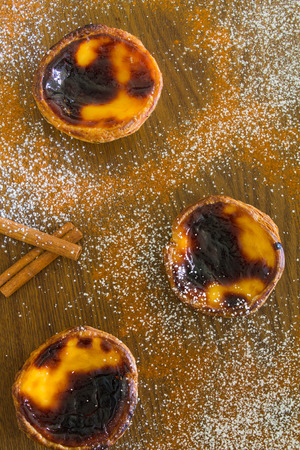 three traditional portuguese egg pies on a wood table with cinnamon and powder sugar
