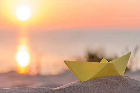 Yellow paper boat on a beach at sunriseの写真素材
