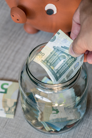 Saving money concept. Man hand inserting euro bill in glass canの写真素材