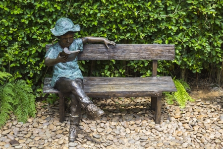 Statue reading a book sitting on bench in gardenの写真素材