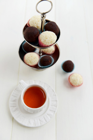 Tea Cup and Homemade Chocolate and Coconut Truffles on White Wooden Background. Very Shallow DOF, focus on upper truffles.の写真素材