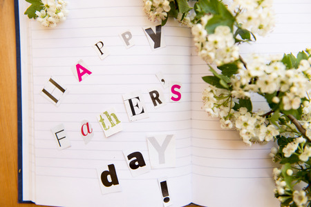 Happy Fathers Day Letters Cut out from Magazine laying on the Notebook with Cherry Blossom Stick nearbyの写真素材