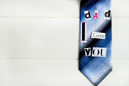 Dad I Love You Letters Cut out from Magazine with Blue Tie laying on White Wooden Backgroundの写真素材