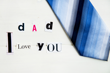 Dad I Love You Letters Cut out from Magazine with Blue Tie laying on White Wooden Backgroundの写真素材