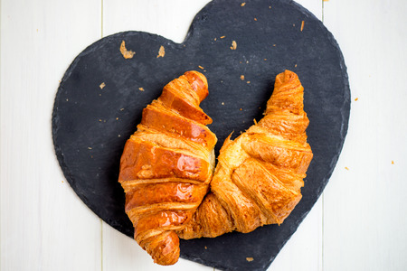 Two Fresh Croissants are ready for the Breakfast and laying on the Heart Shaped Blacked Coaster, Top Viewの写真素材