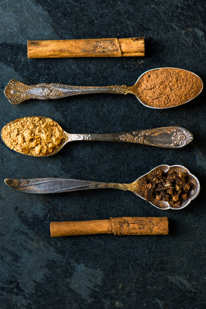 Spices for Christmas Gingerbread Cookies in Spoons on the Dark Grunge Background. Ground Cinnamon, Cinnamon Sticks, Ginger, Cloves, Nutmegの写真素材