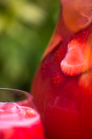 Very Red Fresh Homemade Strawberry and Raspberry Lemonade with Ice Cubes, Mint and Lime in Glass Jar on Green Backgroundの写真素材