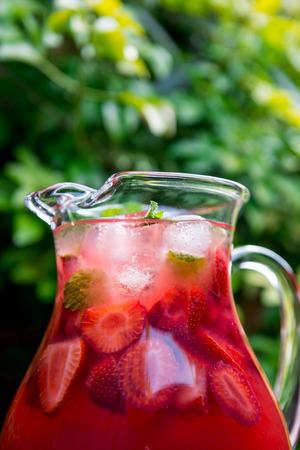 Very Red Fresh Homemade Strawberry and Raspberry Lemonade with Ice Cubes, Mint and Lime in Glass Jar on Green Backgroundの写真素材
