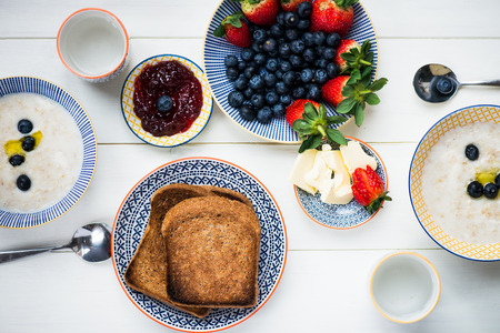Table set for Tasty Family Breakfast with Toasts, Butter, Raspberry Jam, Oat Porridge, Strawberries, Blueberries on White Background, selective focusの写真素材