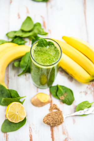 Freshly Made Healthy Green Smoothie from Banana, Spinach, Ginger, Lemon and Flax seeds, White Rustic Background, Ingredients nearbyの写真素材