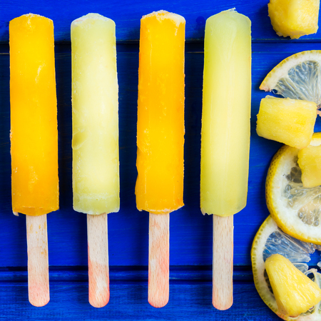 Bright Orange, Pineapple and Lemon Ice Popsicles on the Wooden Blue Backgroundの写真素材