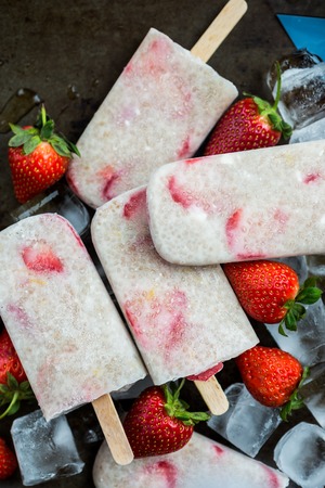 Homemade Vegan Strawberry Popsicles with Chia Seeds and Coconut Milk laying on the Ice Cubes and Strawberries. Summer food conceptの写真素材