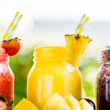 Summer Slushies from Blueberries, Cherries, Lemon, Mango, Strawberries, Lime, Pineapple and Ice with Ingredients nearby, on liht natural backgroundの写真素材