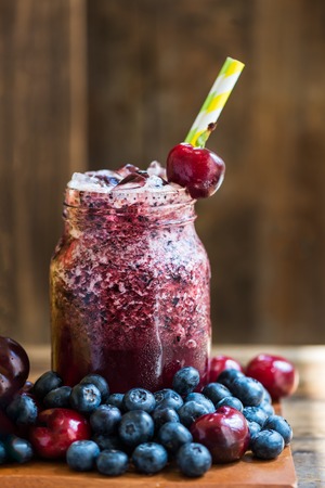 Summer Slushies from Blueberries, Cherries, Lemon, Mango, Strawberries, Lime, Pineapple and Ice with Ingredients nearby, on dark rustic backgroundの写真素材