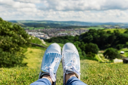 Yound Woman in White Sneakers is relaxing on the Hill with Beautifull View on the city of Llandudno in Nothern Wales during Nice Summer Dayの写真素材