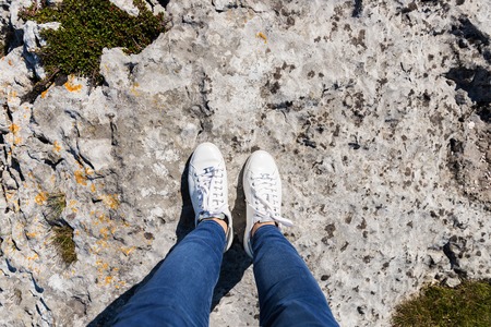 Yound Woman in White Sneakers is making  Photo of her Shoes from above while standing on the big rockの写真素材