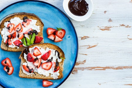Healthy Snack from Wholemeal Bread Toasts, Ricotta cheese and Strawberries with homemade chocolate on the Blue Plateの写真素材
