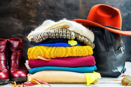Stack of colorful warm autumn and winter clothes with backpack and hatの写真素材