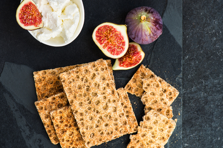 Wholegrain rye crispbread crackers, figs and ricotta cheese are ready for the healthy snack, dark backgroundの写真素材