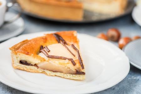 Table set for dessert with all butter pastry case filled with chocolate sauce, almond sponge and pear halves. Decorated with Belgian dark chocolate. Slice of pear cake. Autumn comfort foodの写真素材
