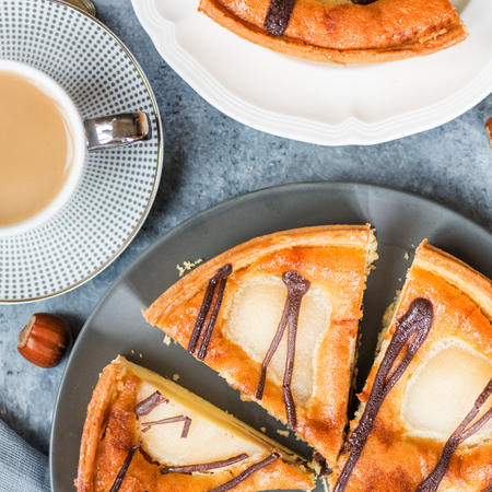 Table set for dessert with all butter pastry case filled with chocolate sauce, almond sponge and pear halves. Decorated with Belgian dark chocolate. Autumn comfort food, top viewの写真素材
