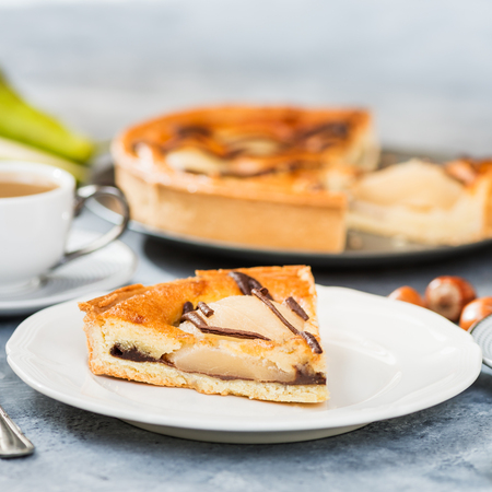 Table set for dessert with all butter pastry case filled with chocolate sauce, almond sponge and pear halves. Decorated with Belgian dark chocolate. Slice of pear cake. Autumn comfort foodの写真素材