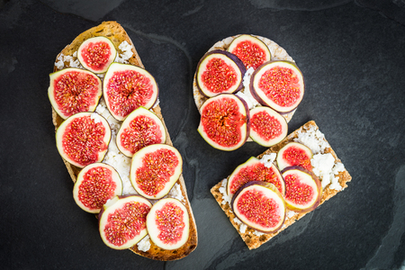 Various Healthy snacks from rice cake, wholegrain rye crispbread crackers and sourdough bread toasts together with figs and ricotta cheese on dark slate boardの写真素材