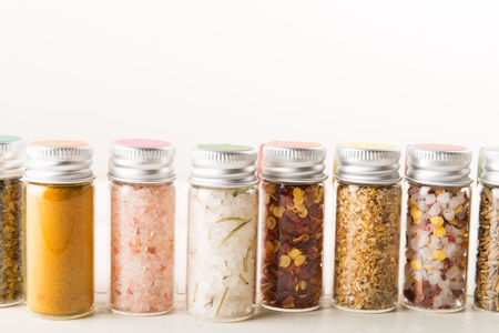 Spices Set in Mini Bottles, such as basil, turmeric, salts, chilli flakes, cumin seeds on light background の写真素材