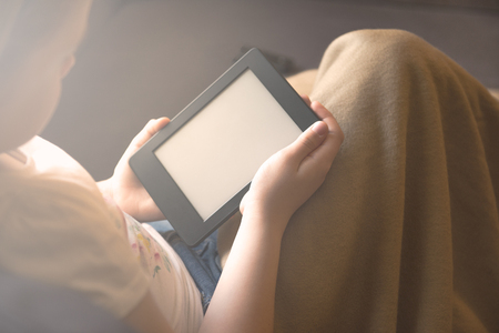 Girl is reading ebook on digital tablet device while relaxing on the sofaの写真素材