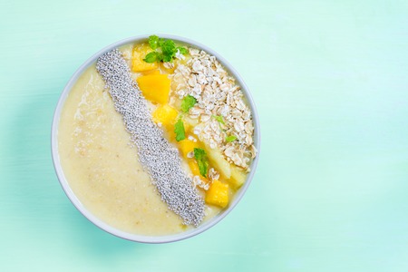 Mango, Banana, Pineapple and Oatmeal Smoothie in the Bowl with Ingredients nearby on the Pastel Blue Background, Top Viewの写真素材