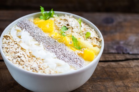 Mango, Banana, Pineapple and Oatmeal Smoothie in the Bowl with Ingredients on top, on the dark wooden backgroundの写真素材
